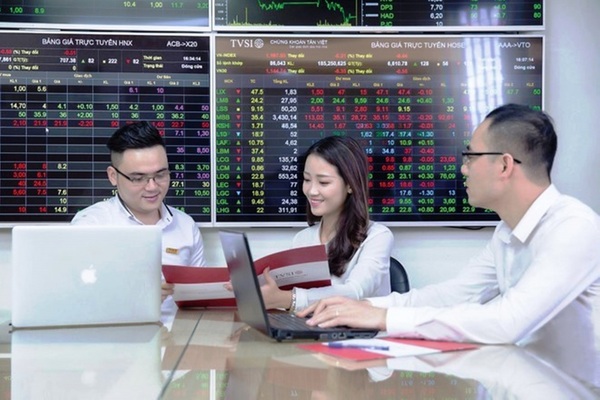 Nhóm nhân viên trao đổi tài liệu bên máy tính và bảng điện chứng khoán.